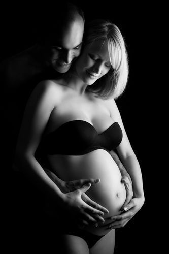 Schwangerschaft Fotografin Düsseldorf: Schwangere mit Partner. Er steht hinter ihr, umfasst mit seinen Händen den Babybauch. Sie legt ihre Hände auf seine.