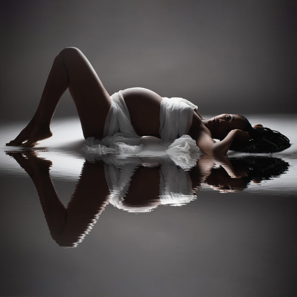 Schwangerschaftsfotografin Düsseldorf. Wunderschöne Schwangere liegend spiegelt sich in Wasser auf dem Boden. Babybauch-Fotografin A. Ola Karlowski